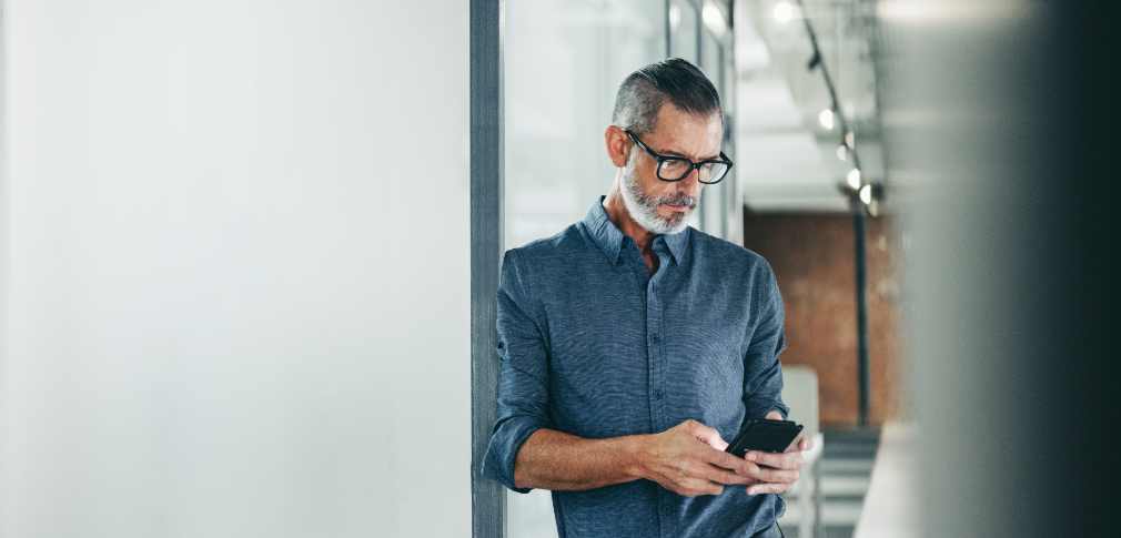 A man is leaning against the wall, looking at his smartphone.