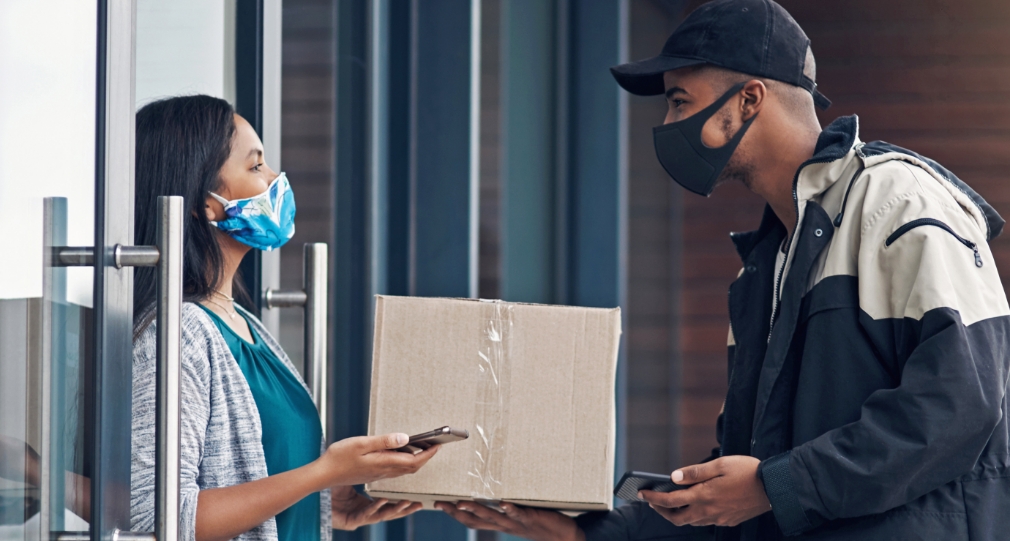 Person standing at a door, receiving a package from another person.