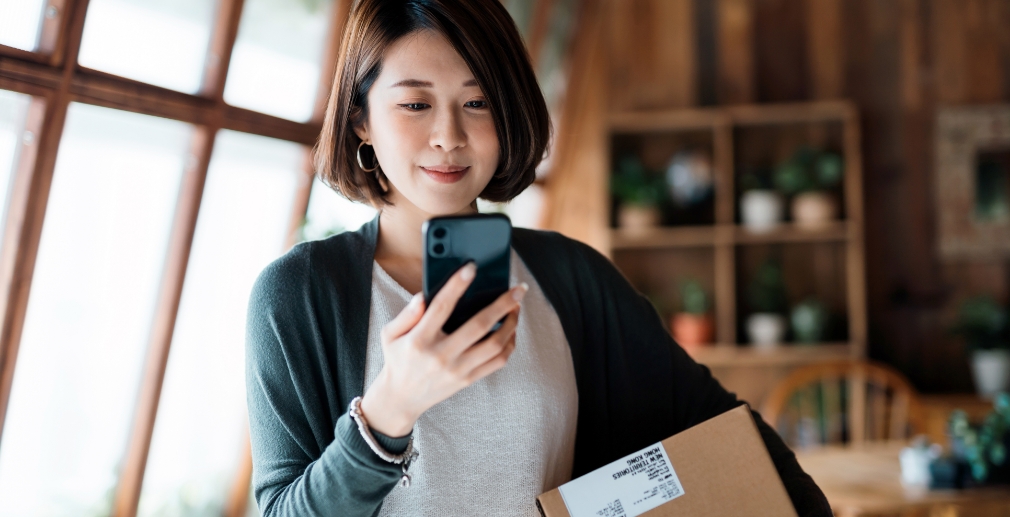 Person holding a package and looking at their phone.