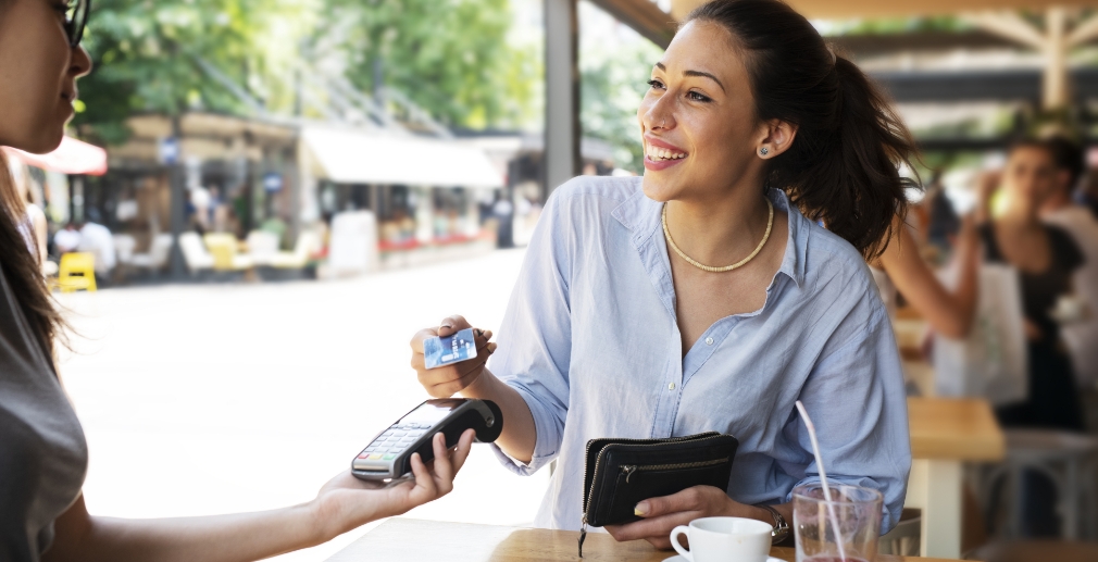Person sitting outside at a cafe, paying for their meal with a credit card.