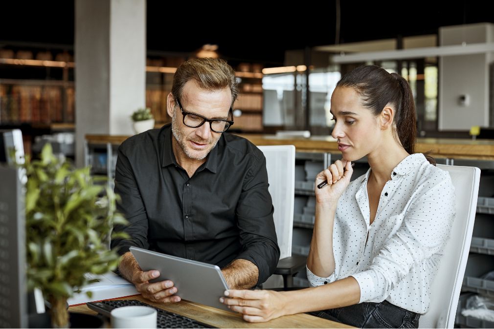 Two people sitting at a table, looking at a tablet together.
