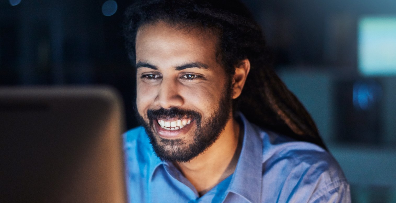 Man wearing a blue shirt looks at his computer and smiles as he discovers he's eligible for the R&D tax credit.