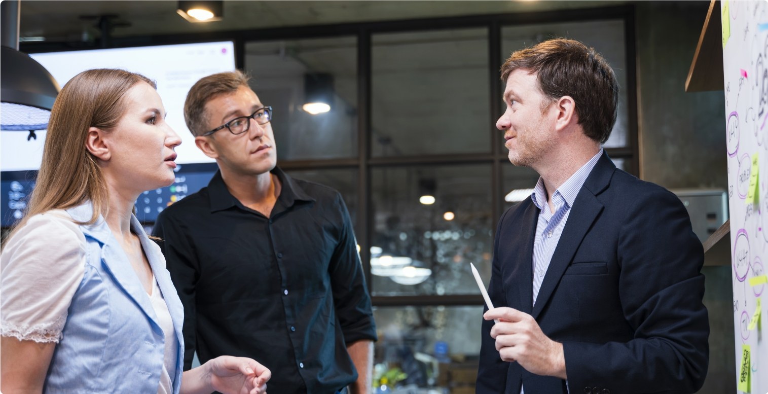 Two men wearing black and one woman in blue stand in their office, debating the pros and cons of becoming a payment facilitator.