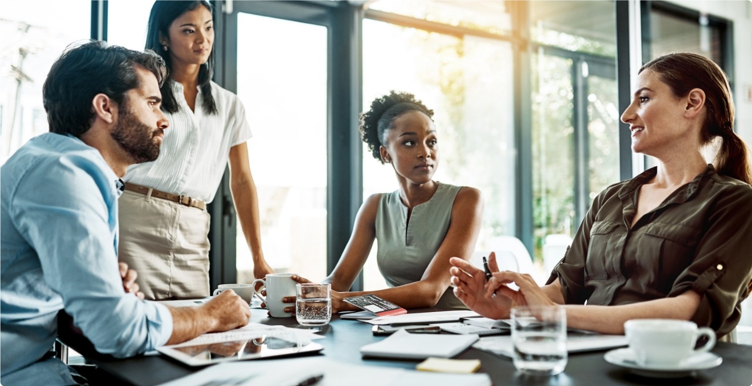 Three women and one man sit around a table covered in papers and notepads, discussing the steps it takes to become a PayFac.