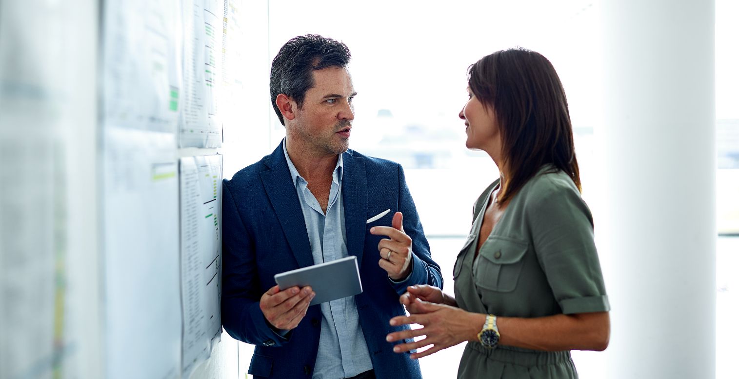 Man in blue suit talks to woman in green dress about an employee management issue.