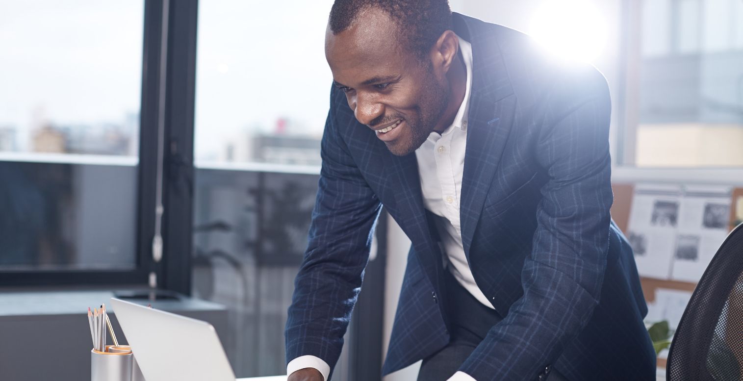 Man wearing blue suit smiles down at his laptop as he connects with a payroll and HR provider.