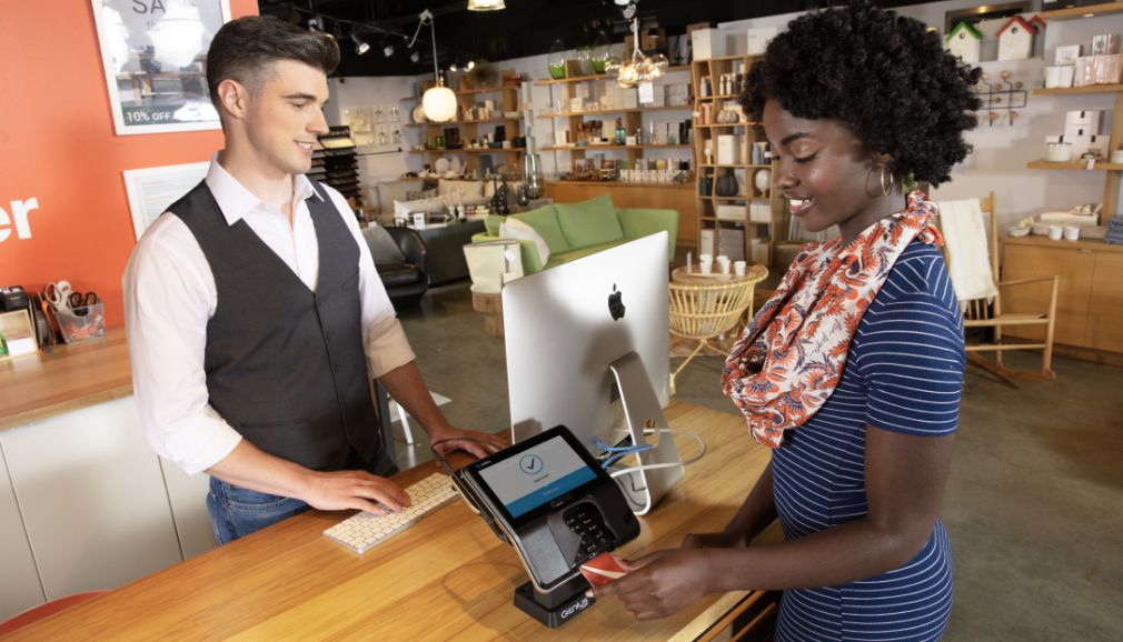 A customer places her credit card into a point of sale device while a store employee stands behind the checkout counter.