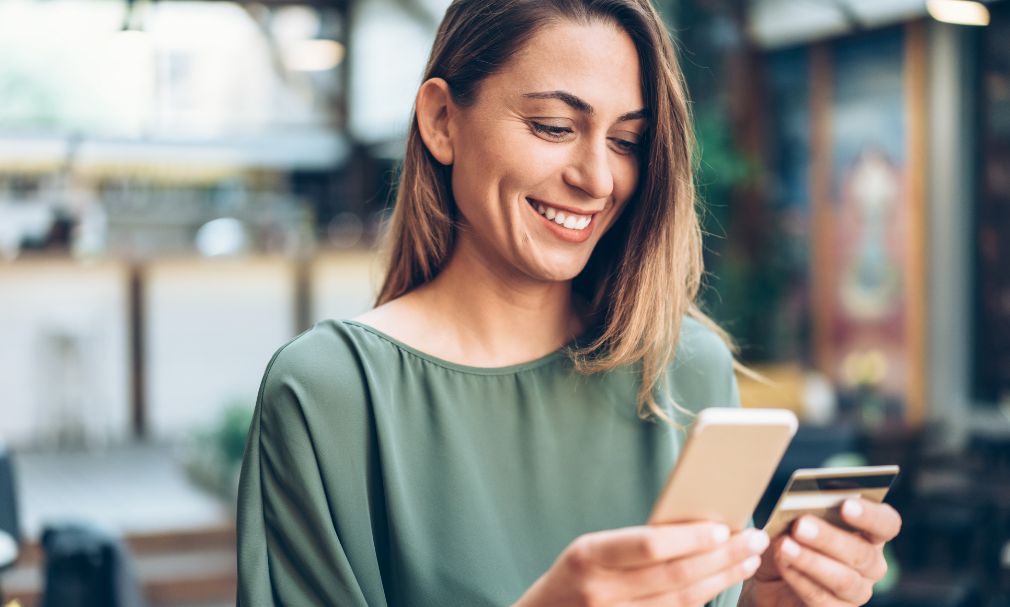 A woman smiles as she enters her credit card information on her smartphone.