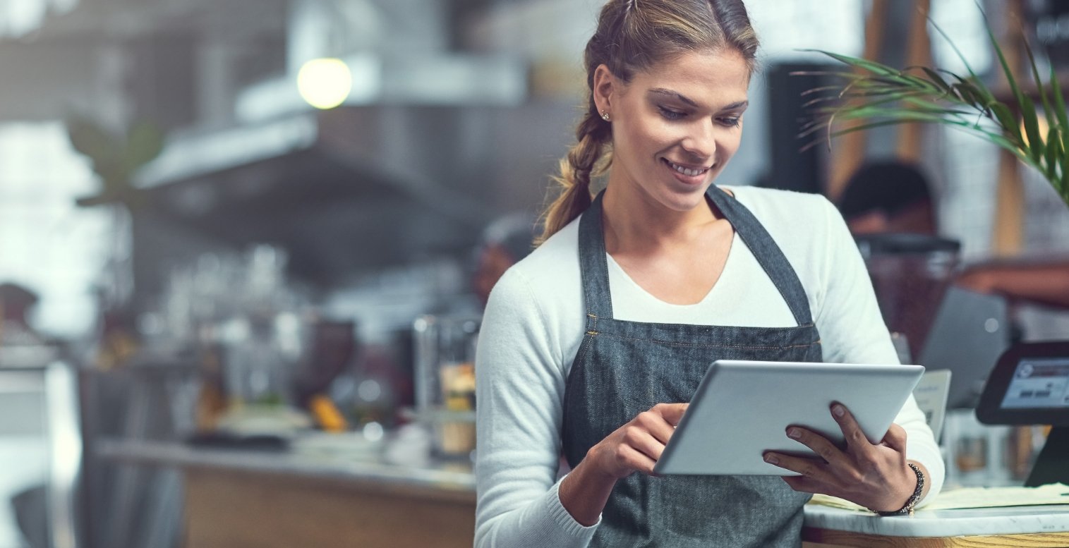 A restaurant employee smiles as she taps on a tablet device.