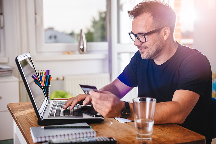 man paying for purchase with credit card at his laptop