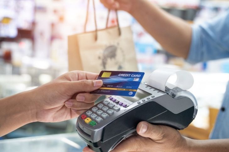 A person holds their credit card over a card reader while the cashier hands them a shopping bag