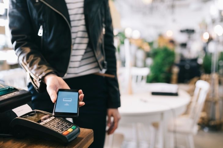 Man taps a smartphone to a contactless card reader at a restaurant