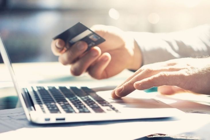 Person holding a credit card in one hand and typing on a laptop computer with the other hand