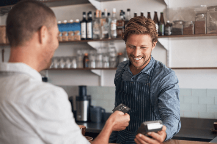A man hands a credit card to a barista holding a card reader