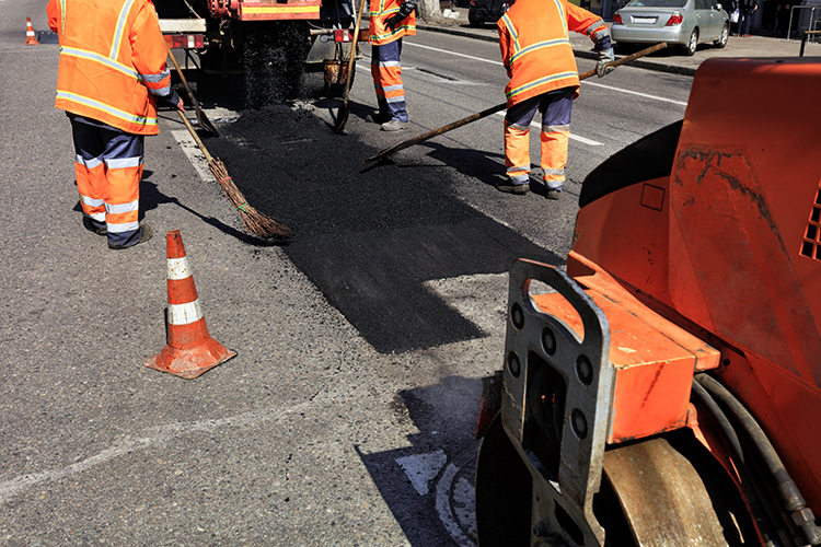 road workers laying asphalt with cones on the side of a road