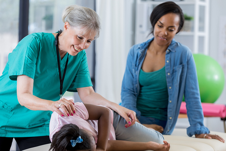 a physical therapist helping a girl with her mother watching