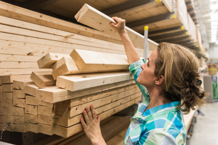 A woman takes lumber off a shelf at a home improvement store.